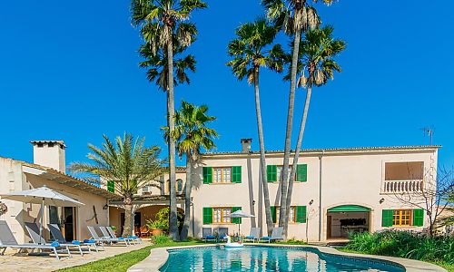 Poolbereich vor der Finca mit Palmen und Rasen und Sonnenliegen